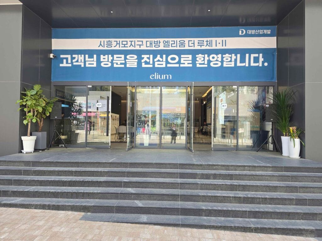 시흥거모 대방엘리움 모델하우스 외부 전경과 환영 현수막이 걸린 메인 출입구