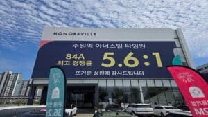 수원역 아너스빌 타임원 모델하우스 옥외 벽면에 대형 글씨로 최고 경쟁률 오점육 대 일 기록이 적힌 현수막과 주차장 전경