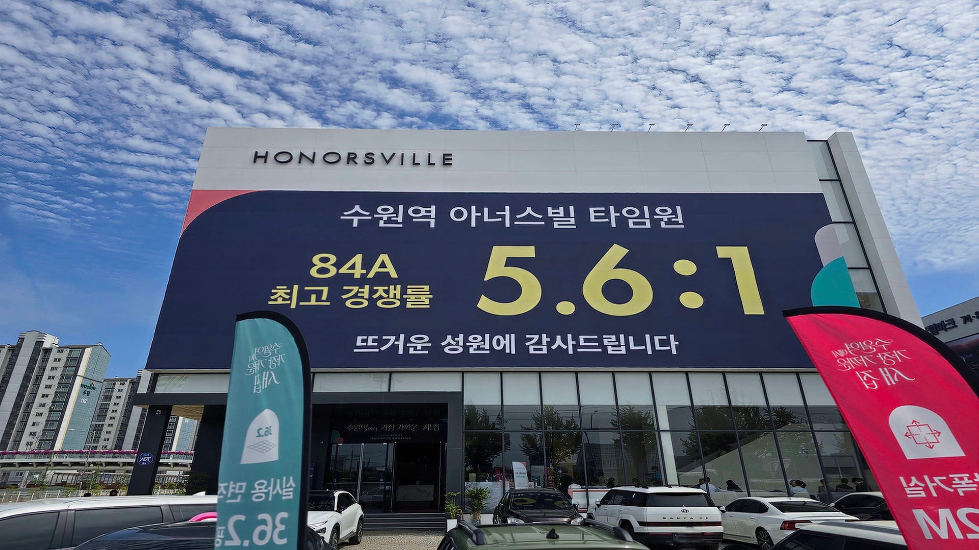 수원역 아너스빌 타임원 모델하우스 옥외 벽면에 대형 글씨로 최고 경쟁률 오점육 대 일 기록이 적힌 현수막과 주차장 전경
